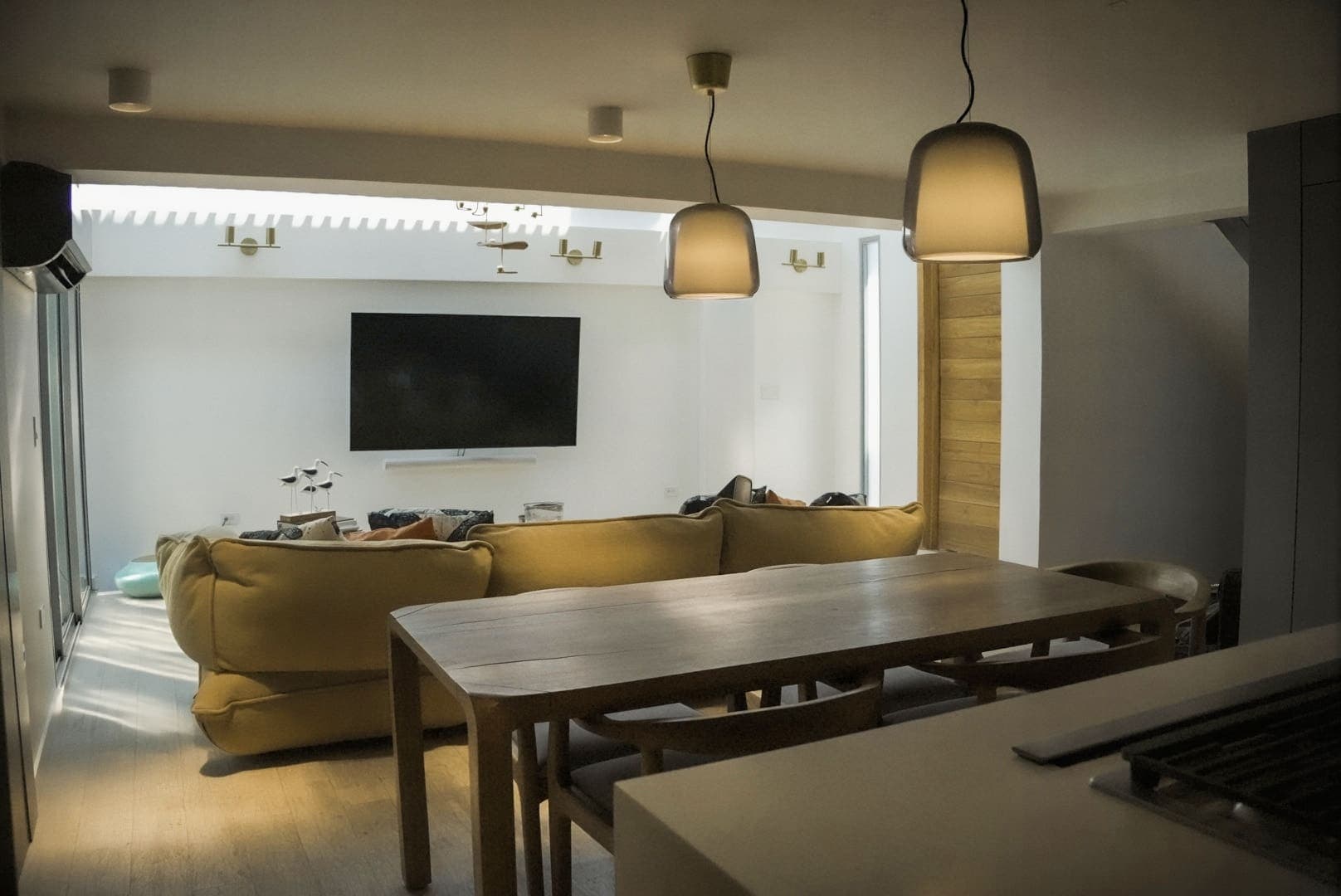 Salón con sofá, televisión y la mesa del comedor bajo lámparas colgantes
